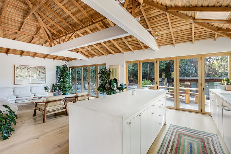 white kitchen with wood folding glass doors and high exposed wood ceiling